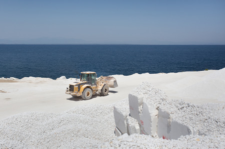 Bulldozer working at white marble quarry on Thassos in Greece, horizon at blue sea in backgroundの写真素材