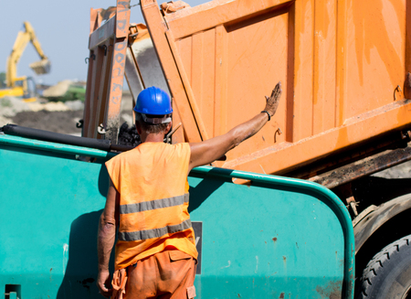 Construction worker showing stop hand sign to his colleague in the truck. Asphalting process at road...