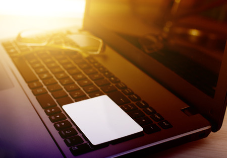 Laptop with white blank business card and eyeglasses on keyboard