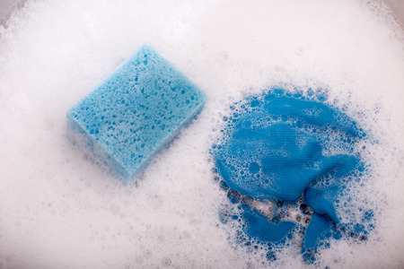 Close up of blue sponge and rag in kitchen sink full of foamの写真素材