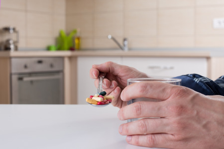 Man holding spoon with many different pills and glass of water at white kitchen tableの写真素材