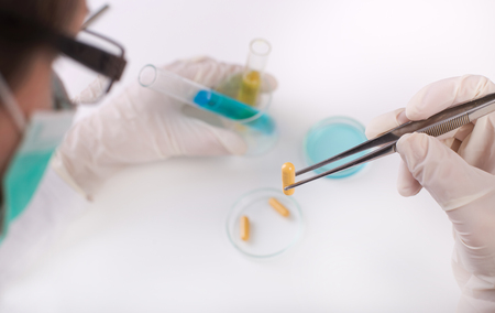 Researcher holding capsule with tweezers above petri dish in the laboratoryの写真素材
