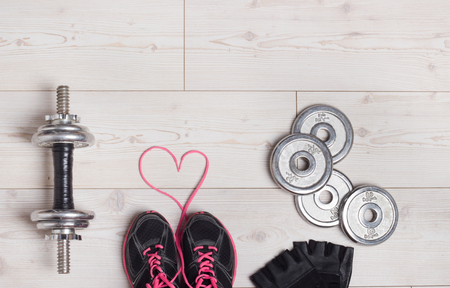 Sport lifestyle concept. Top view of dumbbells, sneakers and sport accessories on the bright wooden floor. Heart shape with shoe lacesの写真素材