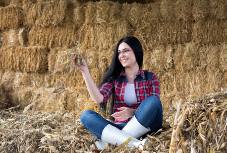 Young pretty country woman sitting in a barn on the straw bales and enjoying lifeの写真素材