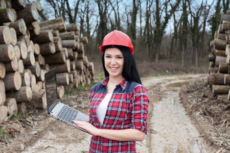 Young female lumber engineer standing with laptop beside cut logsの写真素材