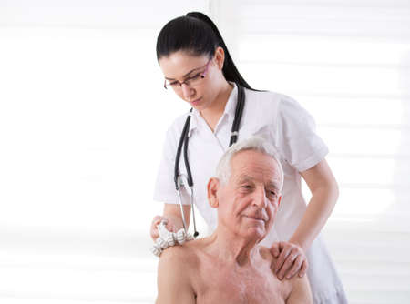 Young pretty practitioner massaging senior man with plastic roller massager