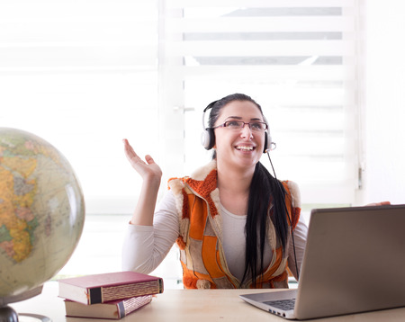 Pretty young student girl with headphones smiling and talking over video call on the laptop at desk