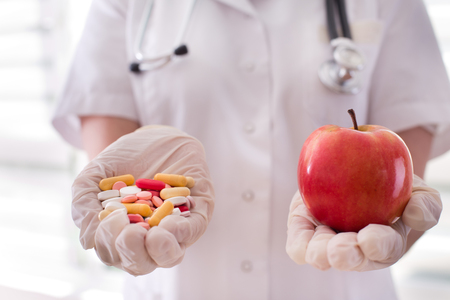 Female doctor holding pile of pills in one and fresh red apple in other handの写真素材