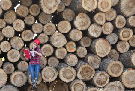 Young woman forestry engineer talking on phone in front of trunks