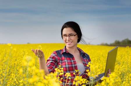 Young pretty woman with laptop in the blooming rapeseed field