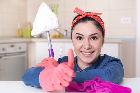Smiling young cleaning lady with pink rubber gloves showing ok sign with thumbs up in the kitchen