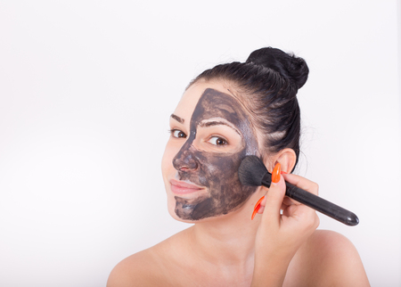 Young pretty woman applying facial mask with brush. Isolated on white background. Skin care and beauty conceptの写真素材