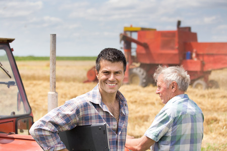 Two farmers standing on field during harvest. Combine harvester working in backgroundの写真素材