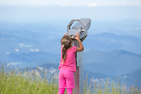 Cute young girl looking through coin operated binoculars from Schneeberg mountain peak in Austriaの写真素材