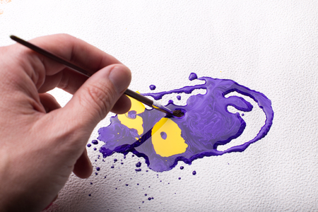 Top view of male hand holding paintbrush and making art from spilled colorsの写真素材