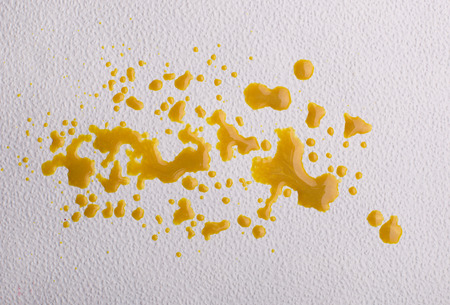 Dripping yellow paint forming abstract blot on white textured backgroundの写真素材