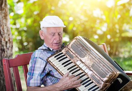 Old man enjoying playing accordion in his gardenの写真素材