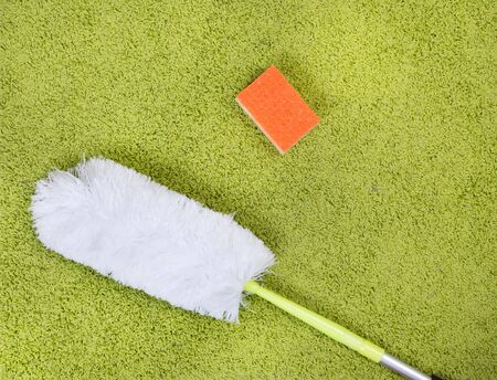 Top view of green fluffy carpet on parquet with duster and orange sponge. Spring cleaning concept