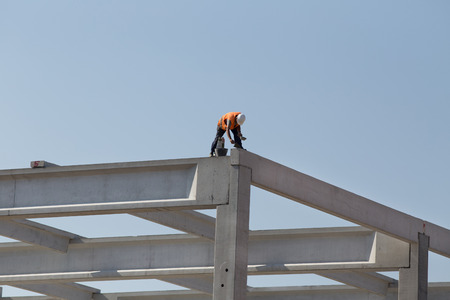 Construction worker without safety equipment working on height, fixing concrete trusses at building...