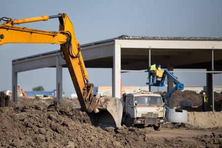 Excavator bucket dredging ground on construction site and workers on cherry picker in background