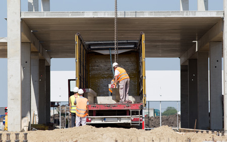 Workers mounting concrete truss on crane hook for lifting at construction siteの写真素材