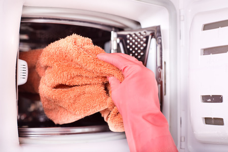 Top view of woman's hand putting towels in washing machine. Laundry job concept