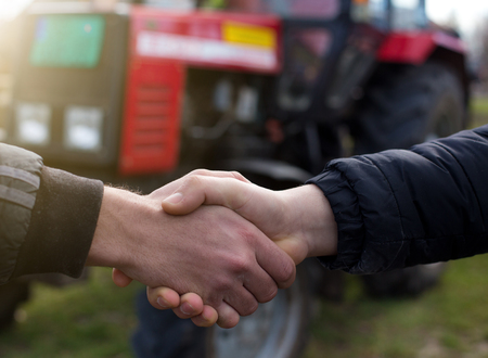 Two farmers shaking hands in front of tractor in fieldの写真素材