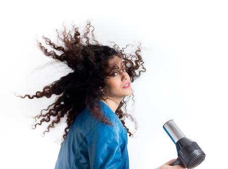 Pretty young girl with long curly hair holding hairdryer. Movement of beautiful curlsの写真素材