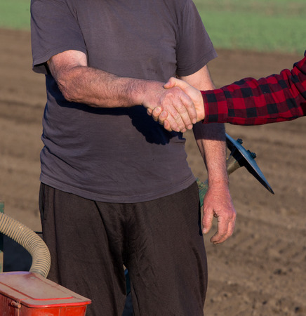 Two farmers shaking hands beside tractor with sowing equipment in field in springの写真素材