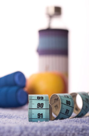 Close up of measuring tape with focus on ideal number for hips with skipping rope, bottle of water and apple in background. Dieting and exercising conceptの写真素材