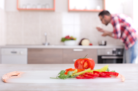 Colorful fresh vegetable on table with handsome man cooking in kitchen in background. Healthy groceries in focusの写真素材