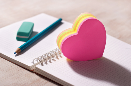 Heart shaped blank stickers on note book with pencil and eraser in background, on wooden desk. Place for your textの写真素材