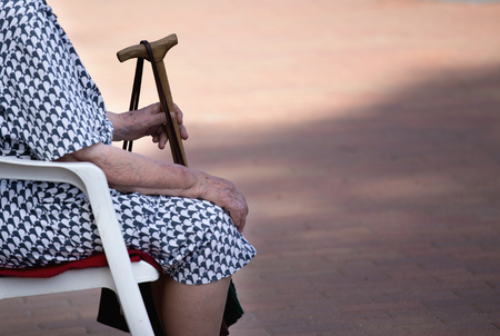 Old woman with wooden stick sitting in parkの写真素材
