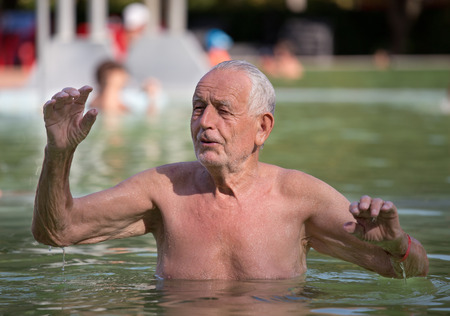 Old man enjoying bathing in outdoor swimming pool with hot water in summertimeの写真素材