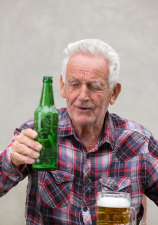 Senior drunk man sitting at table with beer bottle and mug in front of himの写真素材