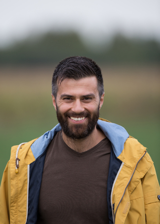 Portrait of young handsome man with beard in yellow raincoat in fieldの写真素材