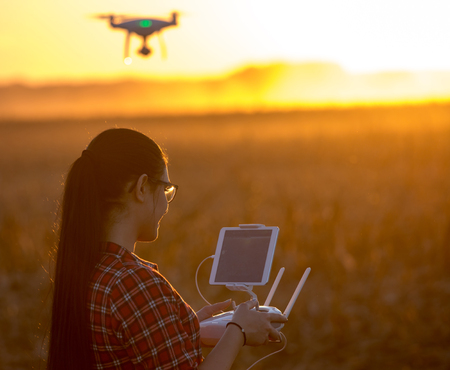 Young farmer woman navigating drone above farmland. High technology innovations for increasing...