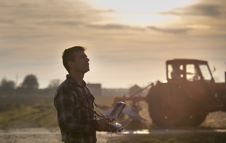 Attractive farmer navigating drone above farmland and looking in the air. High technology...