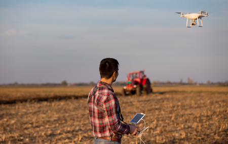 Attractive farmer navigating drone above farmland. High technology innovations for increasing productivity in agricultureの写真素材