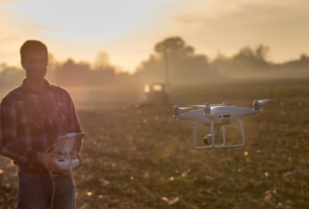 Close up of flying drone and blurred man with remote control in background in field. High technology...