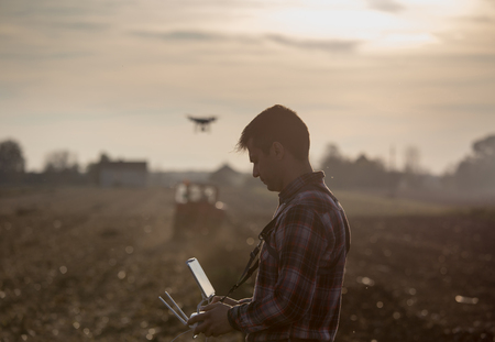 Attractive farmer navigating drone above farmland. High technology innovations for increasing...