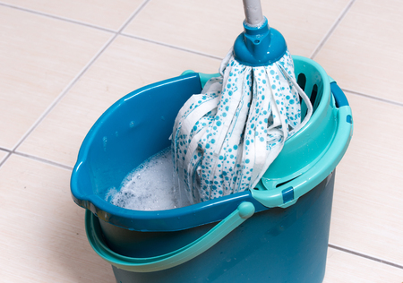 New clean mop squeezing in blue bucket full of foam on tiled floor in kitchen. Housekeeping concept