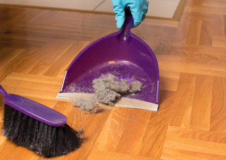Person with protective gloves sweeping parquet floor with small brush and dustpan. Housekeeping concept の写真素材