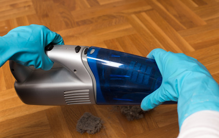 Hands with protective gloves opening handheld vacuum cleaner and removing dustの写真素材