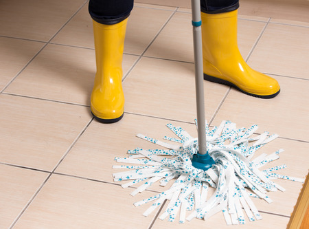 Maid in gumboots mopping tiled floor. Housekeeping and home hygiene conceptの写真素材