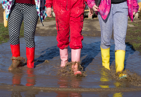 Three young girls in colorful gumboots walking in puddle. Shoes for extreme rainy weather conditions