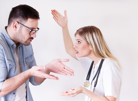 Male patient rejecting to take spoon full of pills from angry female doctorの写真素材