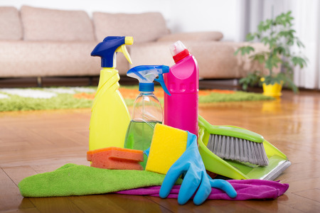 Close up of cleaning products and tools on parquet floor in front of sofa in living roomの写真素材