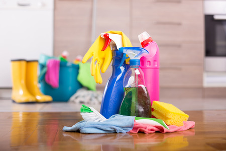Close up of cleaning products and tools on kitchen floor with bucket,  mop and gumboots in front of...