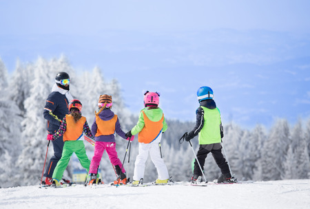Group of kids learning how to ski on slope with instructor. Blue sky and white firs in backgroundの写真素材